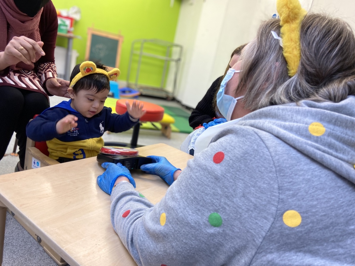 Child playing with a big button, with two adults