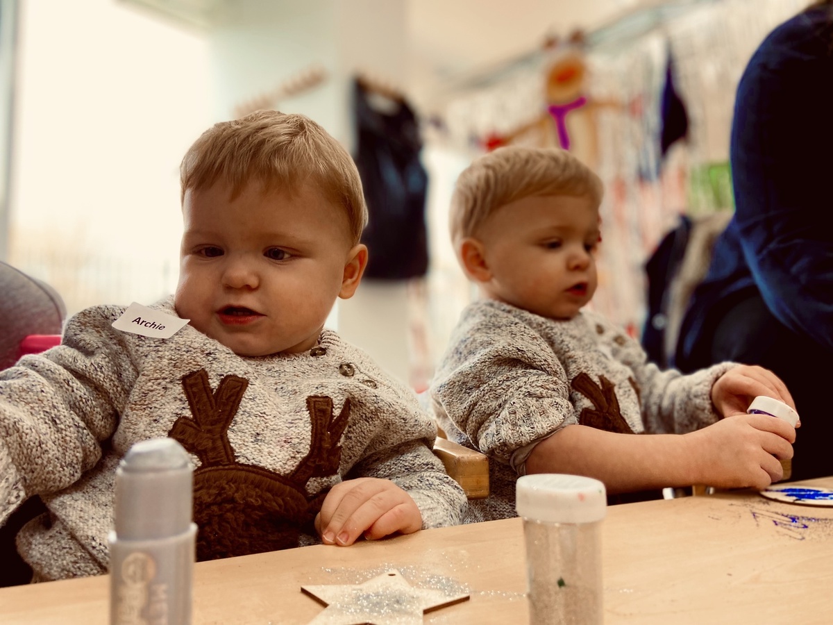 Two twin boys wearing matching outfits, the nearest has a name badge, Archie